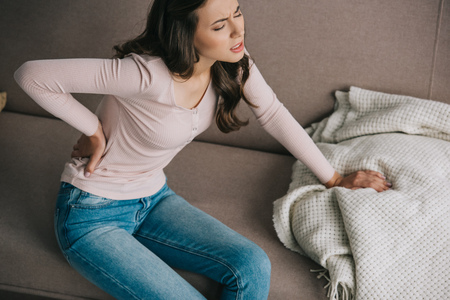 high angle view of young woman suffering from back pain on sofa at home