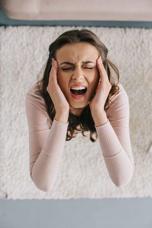 overhead view of young woman screaming and suffering from headacheの写真素材