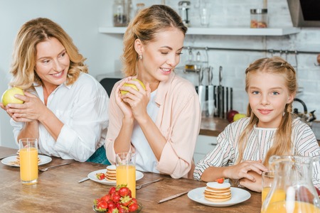happy little child with mother and grandmother having pancakes for breakfast at homeの写真素材