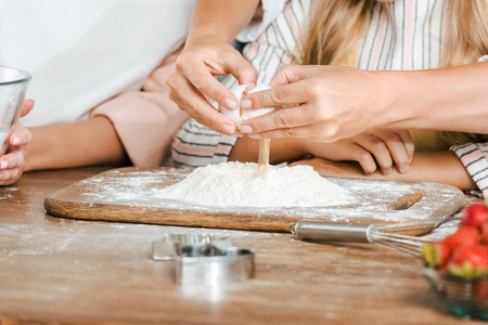 cropped shot of child and women breaking egg into flour for dough on rustic tableの写真素材