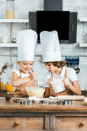 cute smiling children in aprons and chef hats preparing dough for tasty cookies togetherの写真素材