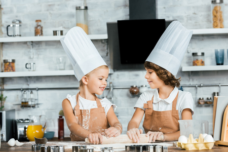 adorable happy kids in chef hats preparing dough for cookies and smiling each otherの写真素材