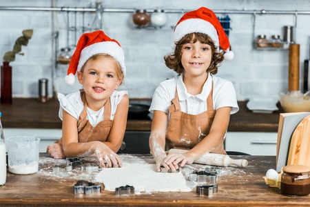 cute happy children in santa hats preparing christmas cookies and smiling at cameraの写真素材