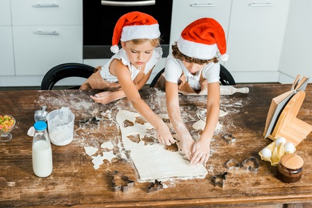 high angle view of adorable chldren in santa hats and aprons preparing christmas cookies togetherの写真素材
