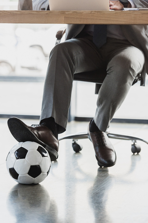cropped shot of young businessman with soccer ball using laptop in officeの写真素材