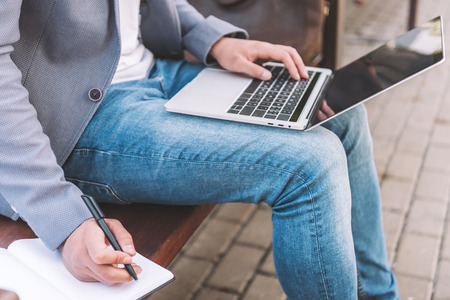 cropped view of freelancer working on laptop and writing in planner while sitting on benchの写真素材