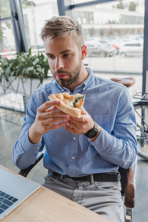 handsome young businessman eating pizza in officeの写真素材