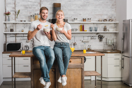 happy couple having breakfast and sitting on kitchen counterの写真素材