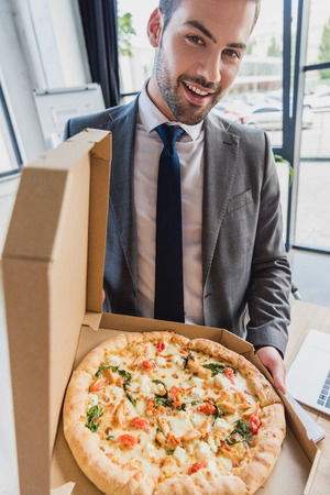 handsome young businessman holding pizza and smiling at cameraの写真素材