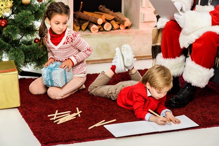 cropped shot of kids unpacking gifts and drawing on floor in front of santaの写真素材