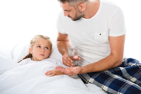 father giving pills and glass of water to ill daughter, isolated on whiteの写真素材
