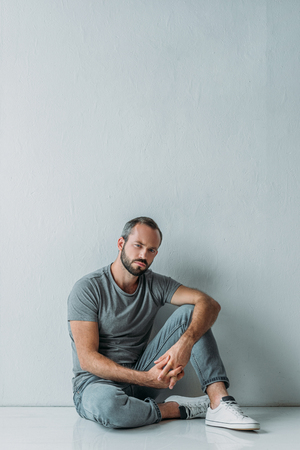 full length view of sad mid adult man sitting on floor and looking at cameraの写真素材