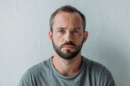 portrait of unhappy bearded man looking at camera on grey