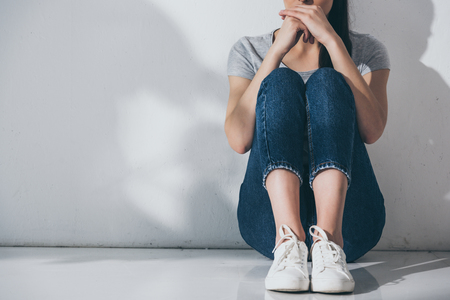 cropped shot of depressed young woman sitting on floor near grey wallの写真素材