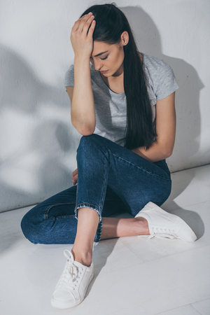 high angle view of stressed young woman sitting on floor with hand on foreheadの写真素材