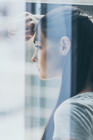 side view of upset brunette woman looking away, view through windowの写真素材