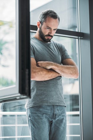 upset middle aged bearded man standing with crossed arms and looking down