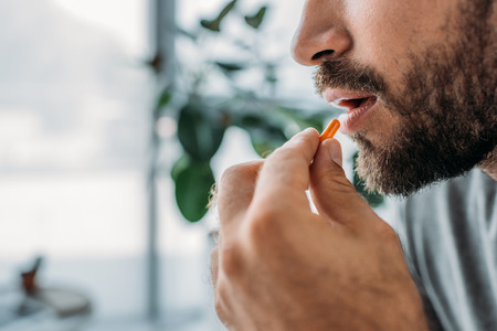 cropped shot of bearded man holding pill near mouthの写真素材