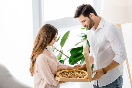 side view of young couple looking at delivired pizza in paper box at homeの写真素材