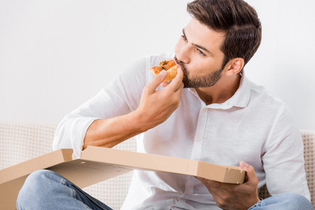 portrait of young man eating pizza alone at homeの写真素材