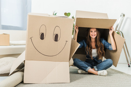 happy woman with cardboard boxes sitting on floor at new homeの写真素材