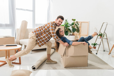side view of smiling couple having fun with cardboard box at new house, moving home conceptの写真素材