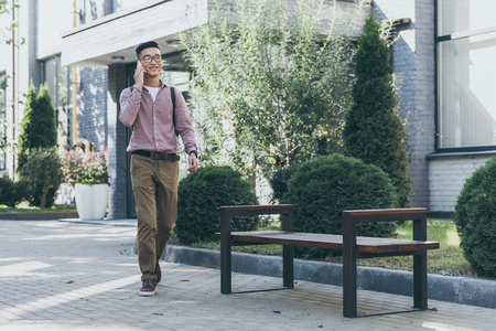 asian man with backpack having conversation on smartphone while walking on streetの写真素材