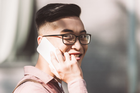 side view of smiling asian man in eyeglasses having conversation on smartphone on streetの写真素材