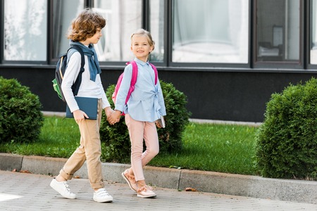 cute little schoolchildren with backpacks holding hands and walking on streetの写真素材