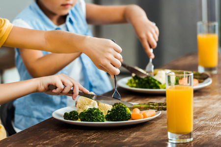 cropped shot of children eating healthy vegetables at wooden tableの写真素材