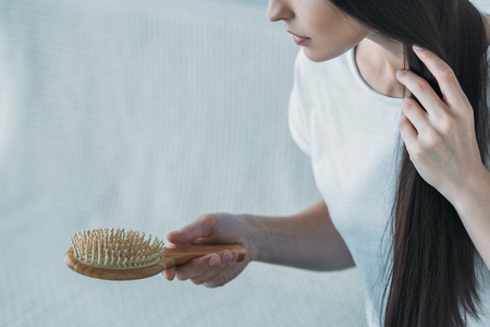 cropped shot of sad brunette woman holding hairbrush, hair loss conceptの写真素材
