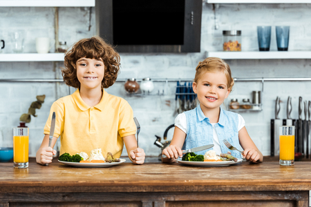 adorable kids eating vegetables and smiling at camera in kitchenの写真素材