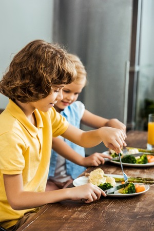 side view of cute happy kids eating healthy vegetablesの写真素材