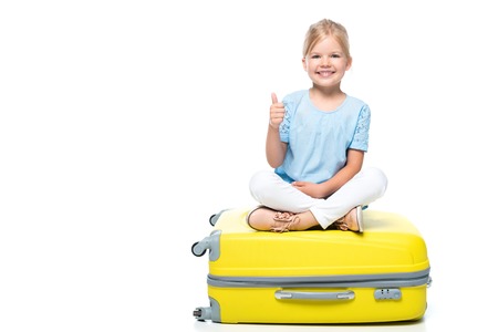 child sitting on yellow baggage and showing thumb up isolated on whiteの写真素材