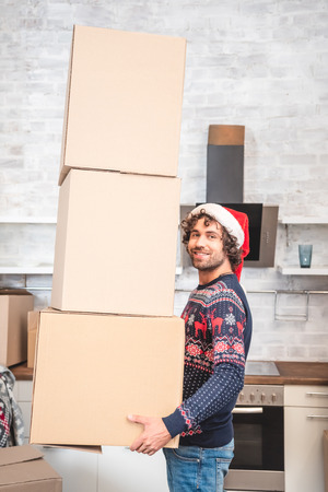 handsome happy man in santa hat holding cardboard boxes and smiling at cameraの写真素材