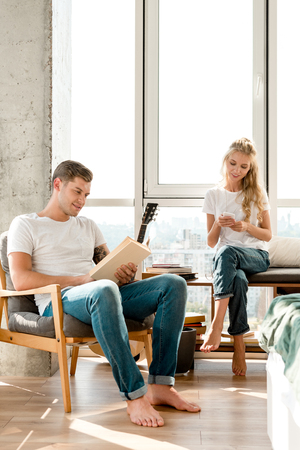 woman using smartphone while boyfriend reading book at homeの写真素材