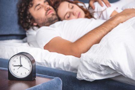 close-up view of alarm clock and young couple sleeping together behindの写真素材