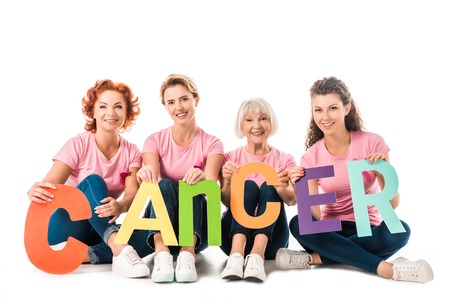 women in pink t-shirts holding colorful letters with word cancer and smiling at camera isolated on whiteの写真素材