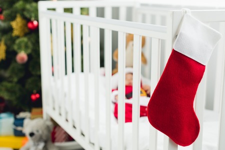 little baby in santa suit lying in crib with christmas gift sock on foreground