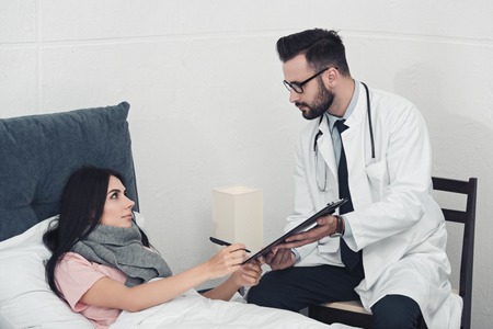 young doctor giving clipboard with documents to patient to signの写真素材