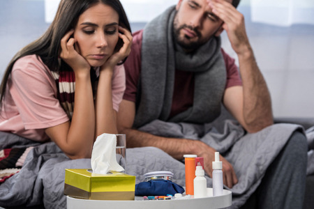 sick couple with meds on table sitting together on couchの写真素材