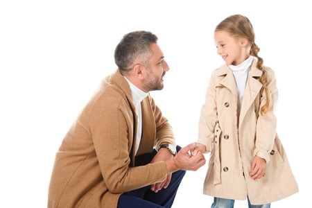 father and daughter in beige coats holding hands and looking at each other, isolated on whiteの写真素材