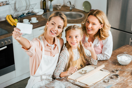 high angle view of woman taking selfie with her mother and daughter while cooking at homeの写真素材