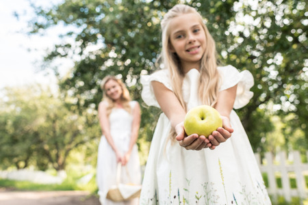 preteen daughter holding apple, young mother with wicker basket on background, selective focusの写真素材