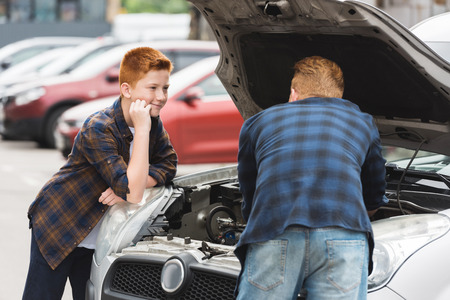 son looking how father repairing car with open hoodの写真素材