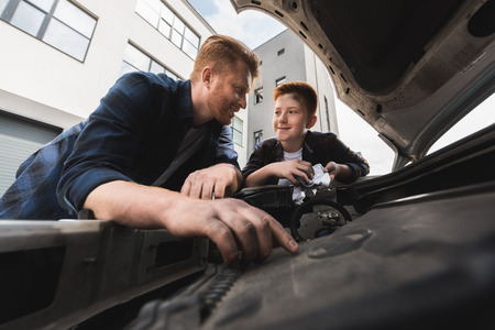 father and son repairing car and looking at each otherの写真素材