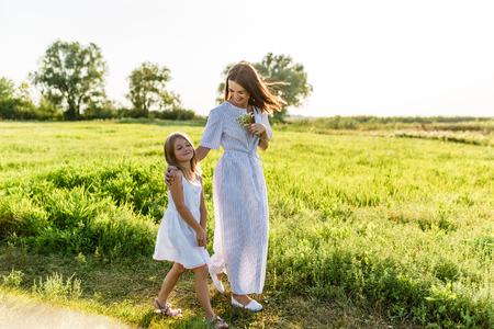 mother and daughter walking together by green field on sunsetの写真素材