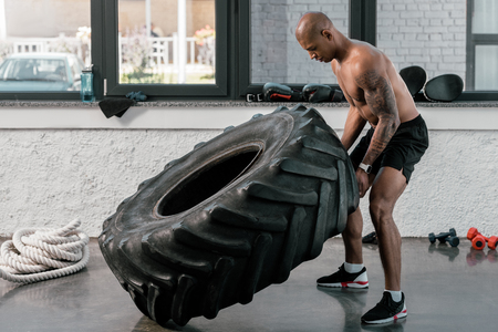 muscular shirtless young african american man exercising with tyre in gymの写真素材
