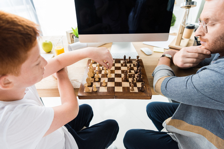 father and son playing chess at table with computer at homeの写真素材