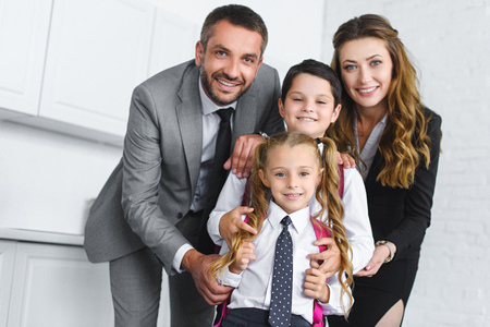 portrait of smiling kids in school uniform with backpacks and parents in suits at homeの写真素材